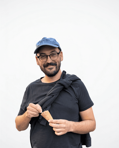 Mann mit Brille und blauer Kappe, hält eine Eistüte in der Hand und lächelt in die Kamera.