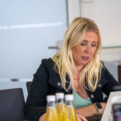 Frau sitzt an einem Tisch und arbeitet konzentriert an einem Laptop in einem modernen Büro.
