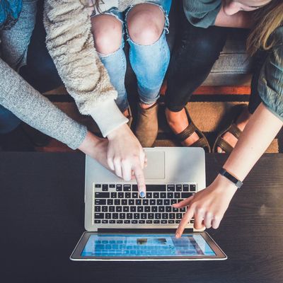 Drei Personen sitzen auf einem Sofa und zeigen gemeinsam auf den Bildschirm eines Laptops.