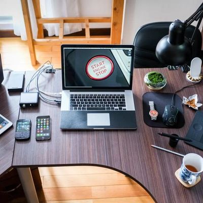 Moderner Schreibtisch mit verschiedenen Elektronikgeräten, darunter ein Laptop, mehrere Smartphones, ein Tablet und Kopfhörer, sowie Bürozubehör wie eine Schreibtischlampe und eine Tasse Tee.