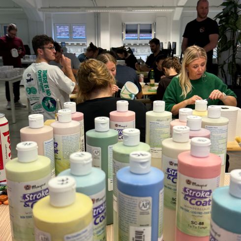 Menschen bemalen Keramik in einem Workshop, viele bunte Farbtöpfe im Vordergrund auf einem Tisch.