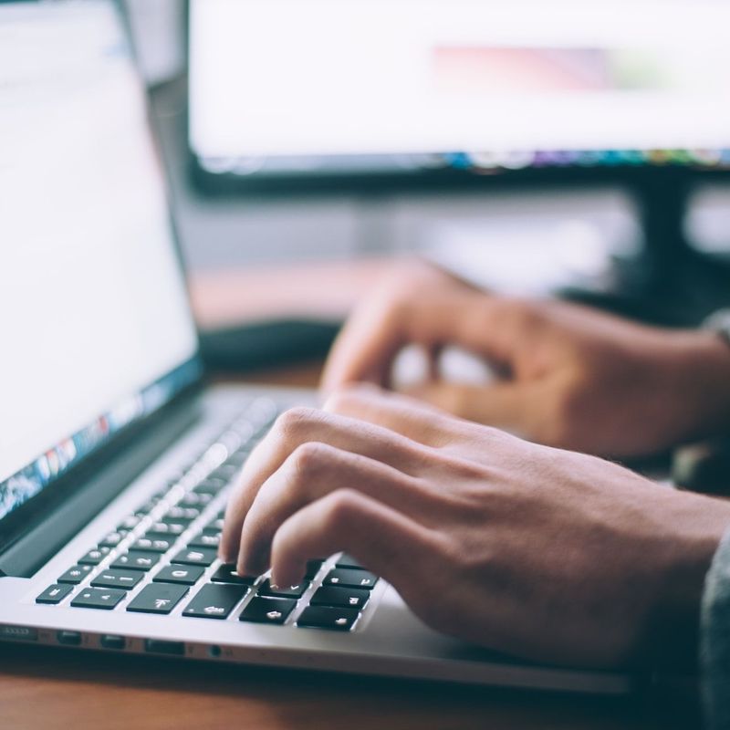 Hände tippen auf einer Laptop-Tastatur, mit verschwommenem Bildschirm im Hintergrund.